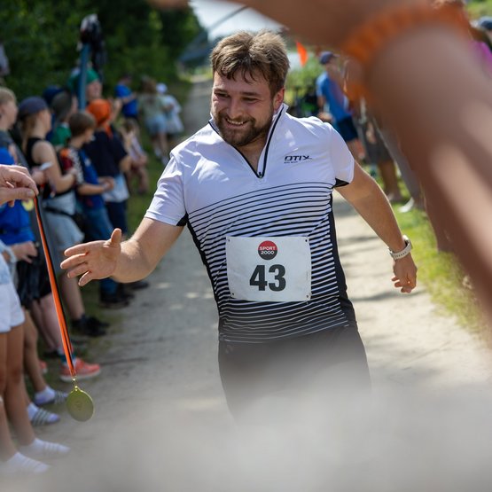 Medaillen gibt es beim Kanal-Cup für alle Teilnehmenden. Ein Teilnehmer läuft ins Ziel und greift nach einer Medaille.