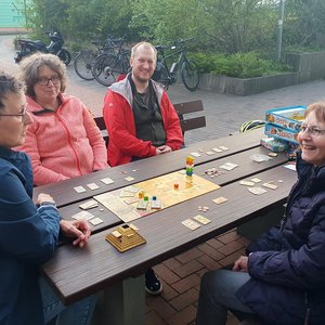 Wegen Renovierungsarbeiten spontan nach draußen verlegt: Kolping-Spieleabend im April. Teilnehmende spielen draußen am Tisch ein Gesellschaftsspiel.
