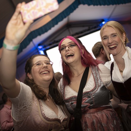 Drei Frauen im Dirndl machen ein Selfie im Festzelt.