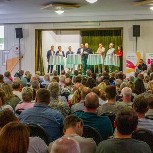 Moderator Andreas Luttmer-Bensmann (4. von rechts) diskutiert mit den Kandidatinnen und Kandidaten, die sich um das Bürgermeisteramt in Wallenhorst bewerben. Blick in den voll besetzten Saal mit der Diskussionsrunde auf der Bühne.